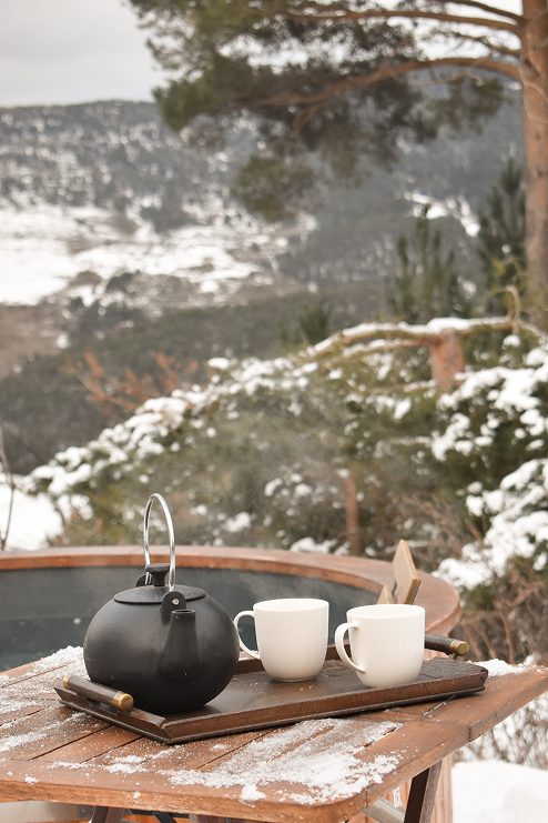 Black teapot and white mugs on a snowy table with mountain views at Minds and Mountains ecolodge