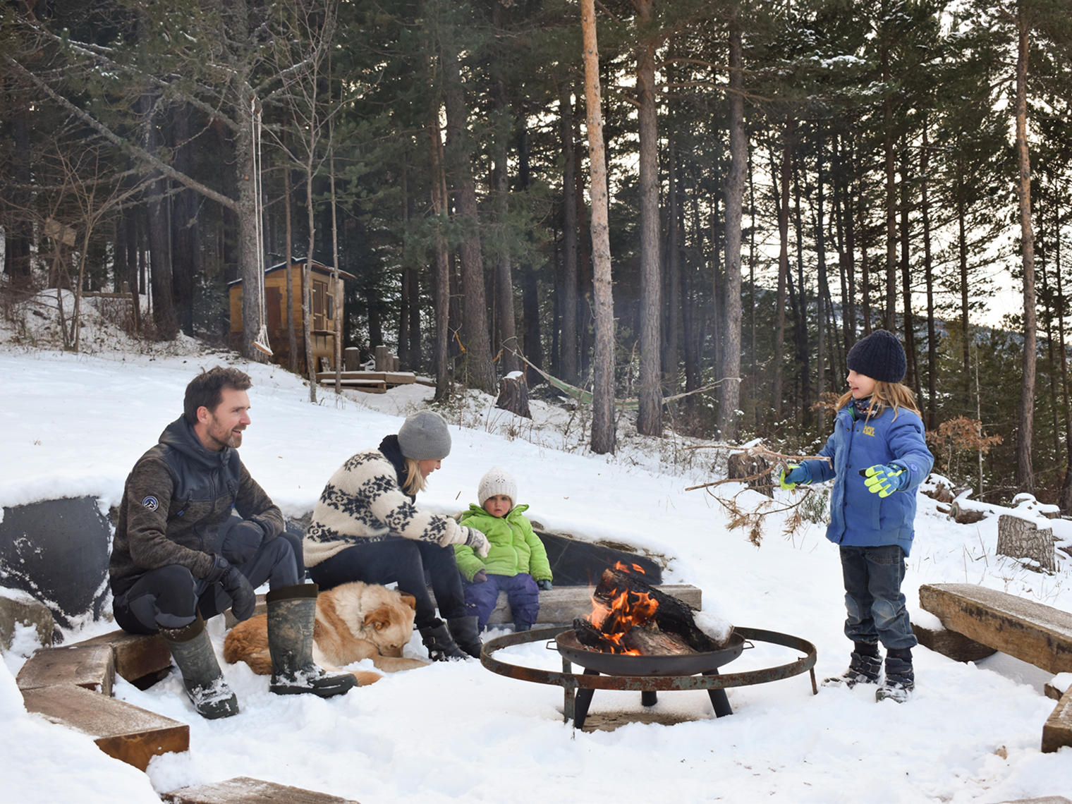 Mikkel-and-Doro-hiking Family with children and a dog gathered around a fire pit in the snow at Minds and Mountains ecolodge